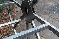 A metal frame is set up on the ground in a city street. It is being assembled with steel parts and tools around. There is a mix of dirt and leaves on the ground, Borken, NRW, Germany [IBR125185857]
