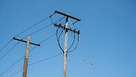 Low angle view of wooden utility poles with overhead power lines and equipment against a clear blue sky [IBR125185864]