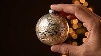 Single aged mercury glass Christmas ornament with faded silver backing and worn gold painted detail held between adult fingers, warm amber bokeh background, nostalgic Christmas memory and heirloom tradition concept, dark warm background, studio shot, AI g [IBR125200737]