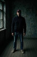 A man stands solemnly in a dimly lit, peeling walled room, creating a mysterious and moody atmosphere, AI generated [IBR125203205]