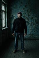 A solitary figure poses in a dim, worn-out room with peeling walls and a window, evoking a moody vibe, AI generated [IBR125203208]