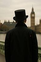 A man in a top hat and black coat stands on a bridge, facing Big Ben in an overcast London setting, AI generated [IBR125203227]