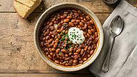 Overhead shot of hearty homemade baked beans with bacon and sour cream in a rustic bowl on a wood table with cornbread, AI generated [IBR125237529]