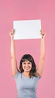 Smiling young woman holding blank sign above head with copy space on pink background [IBR125242401]