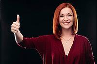 Attractive red haired girl in bordo blouse thinking about something and holding hand with finger up. Young beautiful woman on black background seriously looking at camera. Pretty lady having new idea [IBR125261604]