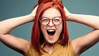 Front view of happy and positivity red haired woman in eyeglasses shouting holding head by hands, looking at camera. Emotionally girl smiling and surprised, having good shock. Drive and happy concept [IBR125261615]