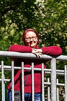 Woman with red hair and glasses wearing a red sweater leaning on a metal railing [IBR125261640]