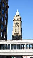 Low angle view of a historic clock tower framed by modern urban buildings against clear blue sky [IBR125280298]