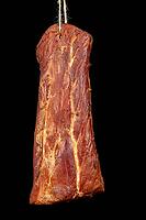 A tasty piece of smoked pork loin hung on a jute string. Stocks in the home pantry. Dark background [IBR125280316]