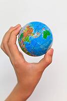 A child's hand holding up a small colored world globe on an isolated background [IBR125324098]