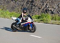 Young beautiful blonde girl in trendy blue jeans and a black T-shirt on the nature behind the wheel of modern motorcycle. Portrait in soft sunny colors [IBR125324100]