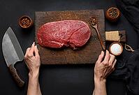 Raw beef tenderloin lies on a wooden cutting board and spices for cooking on a black table, top view and large kitchen knife [IBR125331122]