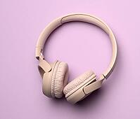Beige wireless headphones on a purple background. Top view on modern gadget [IBR125331124]