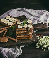 Square French toasts of white bread with chocolate and pieces of banana on a wooden board, vintage toning [IBR125331129]