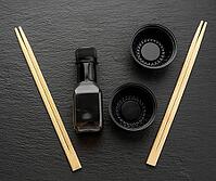 Wooden sticks for sushi, bottle of soy sauce and disposable plastic plates on black background, utensils for delivery [IBR125331142]