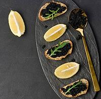 Sandwiches with black sturgeon caviar on a black plate and lemon slices [IBR125331152]
