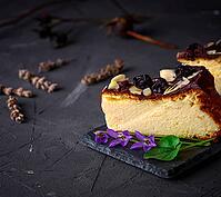 Piece of cheesecake poured with chocolate and almond shavings on a black background, empty space [IBR125331155]