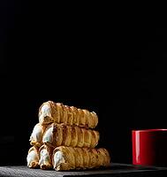 Baked tubules filled with whipped egg whites cream on a black wooden kitchen board [IBR125331160]