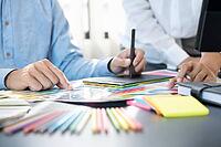 Graphic designer or creative working together coloring using graphics tablet and a stylus at desk with colleague [IBR125331173]