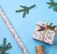 Gift wrapped in pink paper and tied with a brown rope, decor from a green spruce branch on a blue background, top view [IBR125331180]