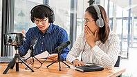 Asian Man and woman podcasters in headphones recording content with colleague talking to microphone and camera in broadcast studio together, communication technology and entertainment concept [IBR125331186]