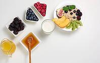 Milk, plate with oatmeal porridge and fruit, freshly squeezed juice in a transparent glass decanter, honey in a bowl on a white table. Healthy breakfast [IBR125331193]
