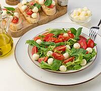 Salad with mozzarella, cherry tomatoes and green lettuce in a white round plate on the table, close up [IBR125331205]