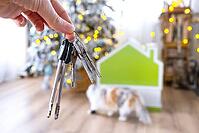 Keys in hand on background fairy lights Christmas tree and tiny house gift and cat for New Year, Christmas. Building, design, project, moving, insurance, mortgage, rent and purchase real estate [IBR125331212]