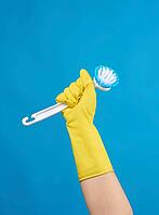 Hand in a yellow rubber glove for cleaning a house holds plastic brush with a handle on a blue background [IBR125344241]