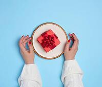 Two female hands holding a plate with a gift on a blue background, top view [IBR125344243]