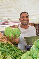 Seller showing to camera different vegetables on his hand in street market India at Jodhpur, India [IBR125344246]