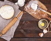 Yeast dough in a wooden bowl on a brown table and ingredients, top view, empty space in the middle [IBR125344263]