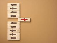 Wooden blocks with brown arrows in one direction and one block with a red arrow in the opposite direction. Concept of difference, uniqueness of thinking, not like everyone else [IBR125344276]