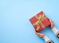 Female hand holds a red box tied with a golden ribbon, concept of congratulations and gifts, top view, blue background [IBR125344291]