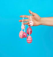 Female hand holds easter colored pink eggs on a rope, blue background [IBR125344295]