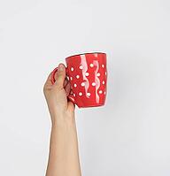 Red ceramic cup in a female hand on a white background, hand is raised up [IBR125344300]
