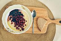 Top view of a plate of wheat porridge with red currants and blueberry jam. A plate of wheat porridge for a healthy gluten-free breakfast, next to a spoon and a piece of bread. [IBR125344317]