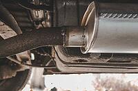 An aftermarket exhaust muffler installed on an older vehicle with signs of welding. automotive element [IBR125363537]