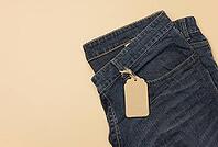 Blank cardboard rectangular tag tied to blue jeans. Top view, copy space [IBR125363538]