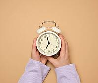 Two female hands hold a round alarm clock, the time is seven in the morning [IBR125363541]