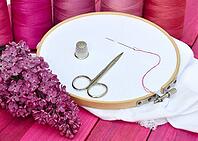 White cloth in wooden embroidered embroidery frame, behind a row of thread reels in red [IBR125363545]