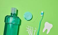 Green toothbrush, mouthwash bottle, dental floss in case, plastic floss holders on green background. Top view [IBR125363573]