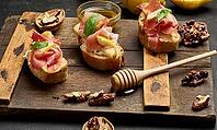 Italian bruschetta with prosciutto, pear slices, cream cheese and fresh basil, garnished with sesame seeds, served on a rustic wooden board [IBR125382560]