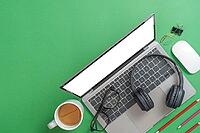 A laptop with headphones, glasses, and stationery on a green background, symbolizing modern learning or remote work [IBR125382577]