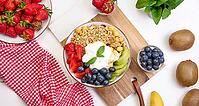 Granola with strawberries, kiwi, banana and blueberries in a round plate on a white table. Healthy and tasty food, top view [IBR125382628]