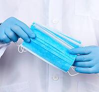 Doctor in a white coat, blue latex sterile gloves holds textile medical masks in his hand, protective accessory against viruses and bacteria, close up [IBR125382641]