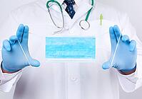 Doctor in a white coat, blue latex sterile gloves holds textile medical masks in his hand on a white background, protective accessory against viruses and bacteria [IBR125382642]