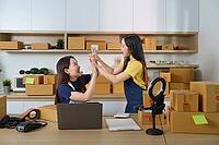 Young woman show joy and teamwork as they complete e-commerce tasks in a lively office environment [IBR125382655]