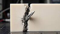 Ceramic solid electrolyte slab, pale ivory surface splitting along a fresh crack with a metallic lithium dendrite pushing through the fracture like a blade through ice. Macro image of real time material failure in battery research with copy space, AI gene [IBR125395913]
