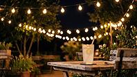 String of Warm Bulbs over a Summer Terrace at Night with Blurred Lemonade Glass, Festive Glow Bokeh Background with Copy Space, AI generated [IBR125395918]
